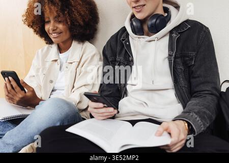 Scatto ritagliato di due studenti universitari che leggono dagli smartphone durante la preparazione degli esami Foto Stock