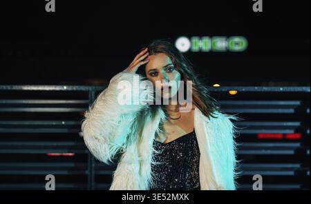 Ritratto di una giovane donna che posa all'aperto di notte indossando abiti eleganti Foto Stock