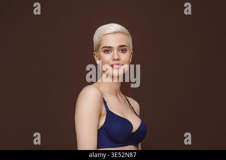 Bella donna bionda con capelli corti in posa su sfondo marrone Foto Stock
