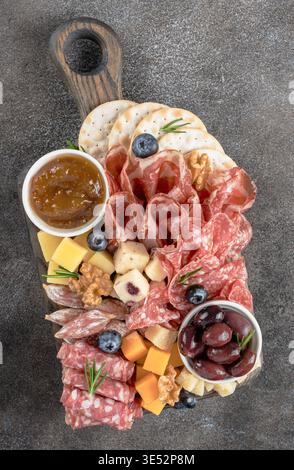 Tagliere di salumi con salumi, formaggi, cracker, marmellata di fichi, noci. Vista dall'alto su sfondo rustico. Foto Stock
