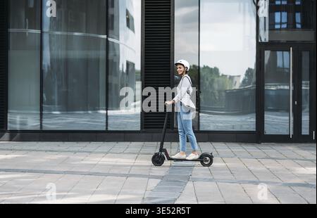 Giovane uomo d'affari che indossa il casco da ciclismo che guida spinga lo scooter sul sentiero Foto Stock