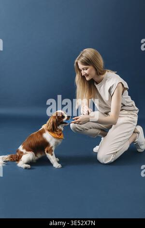 Vista laterale della giovane donna che gioca con il suo cane su sfondo blu Foto Stock