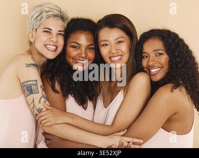 Quattro donne sorridenti diverse che si abbracciano a vicenda. Gruppo di femmine felici di diverse razze Foto Stock