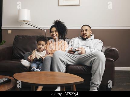 Madre, padre e figlio piccolo che trascorrono il tempo insieme a casa giocando a videogame Foto Stock