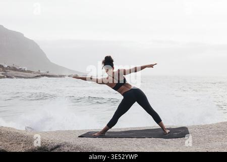 Vista posteriore della donna in forma che fa gli esercizi di riscaldamento sul tappeto da oceano Foto Stock