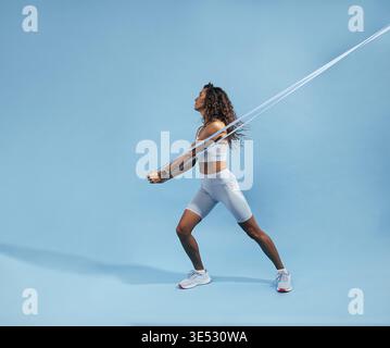 Allenamento femminile con fascia elastica su sfondo blu. Donna atletica sottile che lavora sulla forza del nucleo con la fascia di resistenza Foto Stock