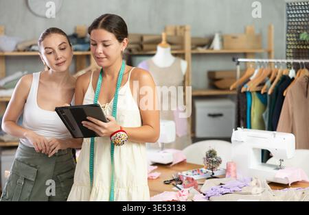 Due sarte che disegnano un modello di vestiti su un tablet Foto Stock