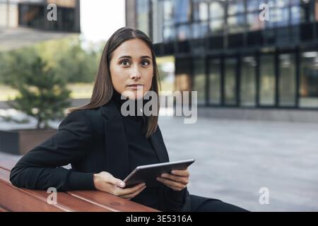 Giovane bruna con tablet digitale. Donna d'affari seduta nel cortile con abbigliamento formale nero Foto Stock