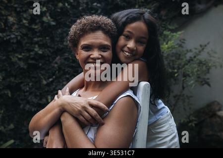 Ritratto di una ragazza e di sua nonna. Nonna seduta su una sedia, nipote che la abbraccia da dietro Foto Stock