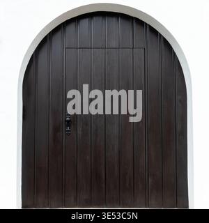 Porta minimale in legno scuro ad arco incorniciata da una parete bianca pulita, fotografata come un semplice dettaglio architettonico in Baviera, Germania. Foto Stock