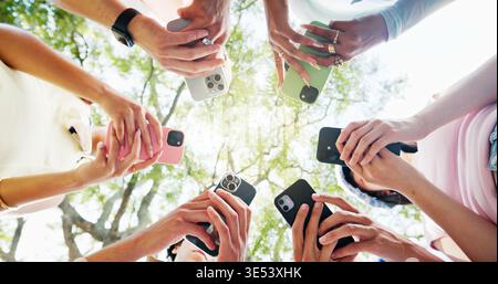 Telefono, cerchio e mani di persone all'aperto con networking, SMS o chat su app mobile. Tecnologia, natura e gruppo di studenti con cellulare Foto Stock
