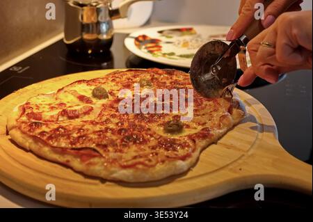 Le mani di donna tagliano la pizza fatta in casa Foto Stock