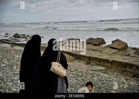 Madre e figlia camminano sulla riva con le onde che si infrangono sulla costa di Breakwater Foto Stock