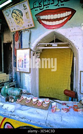 Un dentista di strada lavora a Peshawar. Gli strumenti e i modelli dentali sono visualizzati all'esterno. L'area e' colorata e trafficata. Foto Stock
