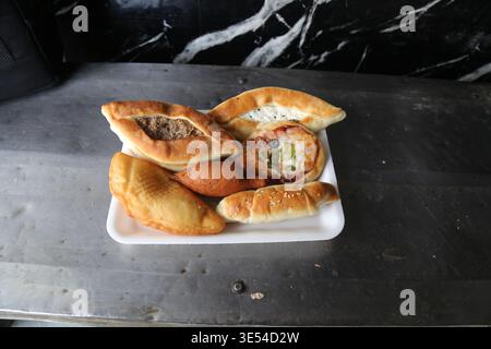 Un piatto di dolci assortiti appena sfornati, tra cui torte di carne, dolci ripieni di formaggio e spuntini fritti, esposti su una superficie metallica, evidenziando Foto Stock
