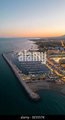 Vista aerea del porto turistico di Puerto Banus con yacht di lusso ed edifici illuminati sul lungomare al crepuscolo a Marbella, Andalusia, Spagna. Foto Stock