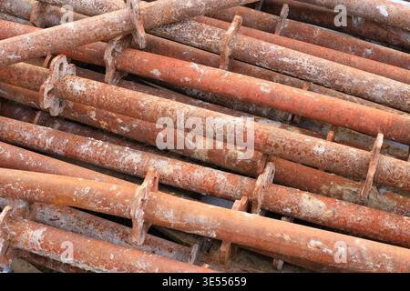 Pali per ponteggi in acciaio arrugginito impilati in un cantiere. Supporti in metallo industriale con guarnizioni con flange, che mostrano segni di uso intensivo e ossidati Foto Stock