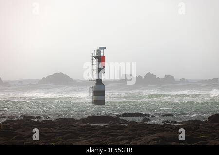 Vista di un faro marittimo a strisce bianche e nere con una cima rossa in mare frastagliato con onde e costa rocciosa a Penmarch, Bretagne, Francia. Foto Stock