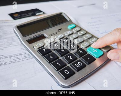 Kirov, Russia - 18 marzo 2026: Una persona utilizza una calcolatrice per gestire le finanze della famiglia e calcolare le spese mensili durante la revisione dei documenti Foto Stock
