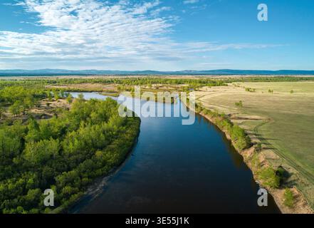La vista panoramica di un tortuoso fiume scorre attraverso vaste praterie e foreste sotto un cielo primaverile limpido Foto Stock