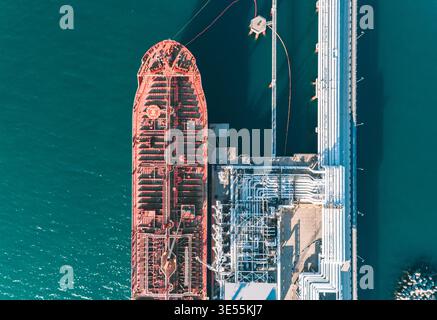 Veduta aerea dall'alto verso il basso di una grande petroliera ancorata a un molo del porto in fase di carico. Foto Stock