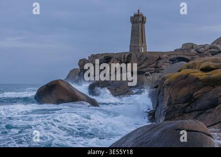 Veduta del faro di Ploumanac'h che sorge su rocce di granito rosa con onde che si infrangono contro la riva e un ponte di pietra a Perros-Guirec, Bretagne, fra Foto Stock