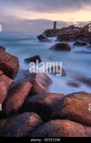 Veduta del faro di Ploumanaca'h che sorge su rocce di granito rosa con lunghe onde nebbiose a Perros-Guirec, Bretagna, Francia. Foto Stock