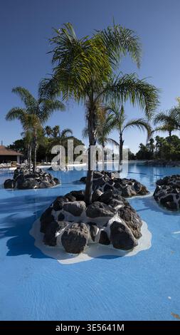 Vista di una grande piscina blu con isole di roccia artificiale e palme sotto un cielo limpido a Ceuta, Ceuta, Spagna. Foto Stock