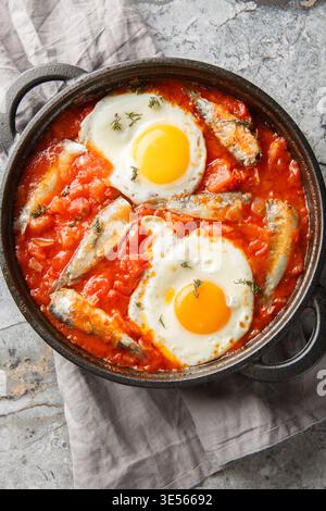 Uova fritte con sardine in scatola e verdure sospese in salsa di pomodoro da vicino in una padella sul tavolo. Vista dall'alto verticale Foto Stock