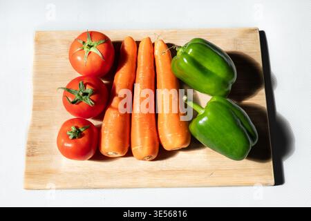 Verdure biologiche fresche assortite, tra cui pomodori rossi, peperoni verdi e carote arancioni disposte su piatti bianchi e taglieri in legno, m Foto Stock