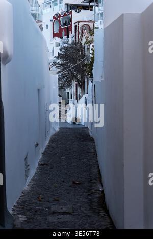 Fira, Santorini, Grecia - 7 ottobre 2025 - Uno stretto sentiero si snoda verso il basso tra edifici bianchi luminosi a Fira, lastricati di ciottoli. Foto Stock