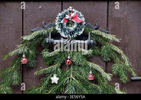 Elegante corona naturale di Natale fatta di coni di pino, frutti di bosco e rami di abete appesi su una porta di legno. Saint Gervais. Francia. Foto Stock