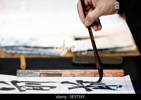 Primo piano di una mano che regge un pennello calligrafico con caratteri cinesi audaci su carta a griglia. Hanoi. Vietnam. Foto Stock