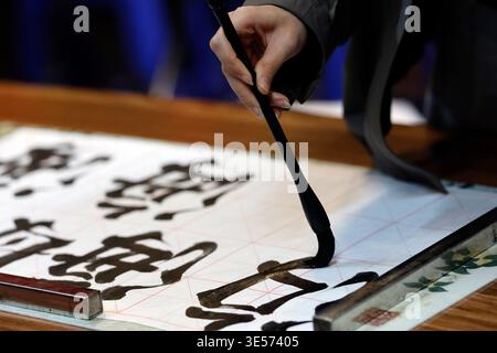 Primo piano di una mano che regge un pennello calligrafico con caratteri cinesi audaci su carta a griglia. Hanoi. Vietnam. Foto Stock
