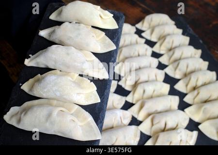 Gnocchi cinesi crudi che mostrano tecniche di piegatura contrastanti disposte su una superficie di ardesia nera. Foto Stock