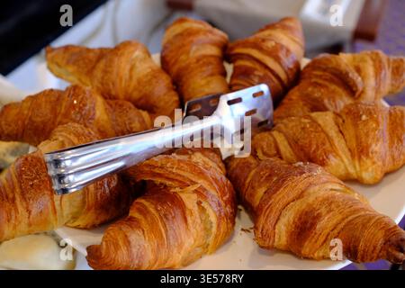 Croissant semplici appena sfornati disposti a grappolo, pinze posizionate su un elegante piatto in porcellana rifinita in viola. Sopot. Polonia. Foto Stock