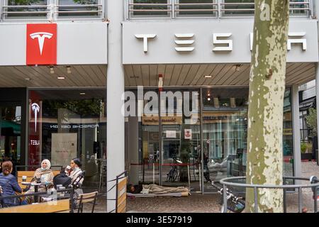 L'esterno di una concessionaria di veicoli elettrici Tesla presenta il caratteristico logo rosso Tesla e la segnaletica stilizzata del nome dell'azienda su un edificio moderno Foto Stock