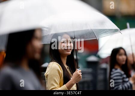 Giovane donna vietnamita sorridente che tiene in mano un ombrello trasparente sotto la pioggia all'aperto. Hanoi. Vietnam. Foto Stock