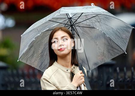 Giovane donna vietnamita sorridente che tiene in mano un ombrello trasparente sotto la pioggia all'aperto. Hanoi. Vietnam. Foto Stock