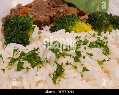 Una foto macro di un pasto preparato con soffice riso bianco guarnito con erbe verdi fresche tritate finemente, probabilmente prezzemolo o. Foto Stock