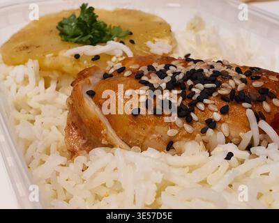 Vista ravvicinata di un pasto da asporto servito in un contenitore di plastica bianco, caratterizzato da una coscia di pollo arrosto dorata ricoperta da bianco e nero Foto Stock