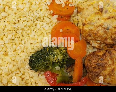 Vista ravvicinata dall'alto di un pasto preparato con riso bianco cotto, carote d'arancia affettate, fiori di broccoli verdi, strisce di peperone rosso, e. Foto Stock
