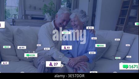Coppia di anziani sorridente che si appoggiano l'uno verso l'altro sul divano luminoso di casa, mostrando notifiche social Foto Stock