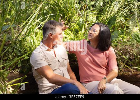 Diverse coppie sedute vicino a un cespuglio basso nel parco, donne che indossano occhiali, entrambi vestiti casual Foto Stock