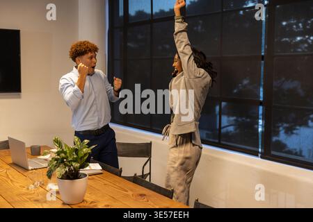 Colleghi afroamericani in tute che fanno il tifo nella sala riunioni con microfono per laptop e cuffie Foto Stock