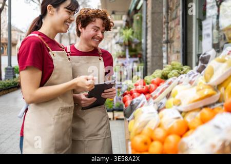 Due assistenti sorridenti del negozio si trovano in un vivace negozio di frutta, organizzando allegramente prodotti freschi. Il luminoso display di frutta colorata mette in risalto il Foto Stock