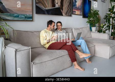 Una coppia di sposi rilassata sta progettando un rinnovo, scegliendo nuovi mobili e tessuti online sul laptop. Foto Stock