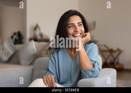 Donna pensiva in abiti casual che si rilassa in un accogliente soggiorno Foto Stock