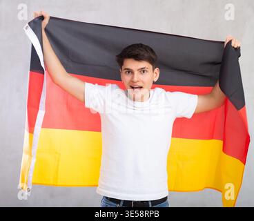 Lo spettatore maschile entusiasta e attivo tiene in mano la bandiera nazionale della Germania e canta slogan popolare Foto Stock
