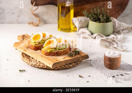 Due fette di pane a lievitazione naturale croccante ricoperte di purè di avocado e uova sode soffici con tuorli che cola. La fotografia del cibo luminoso è caratterizzata da un carattere naturale caldo Foto Stock